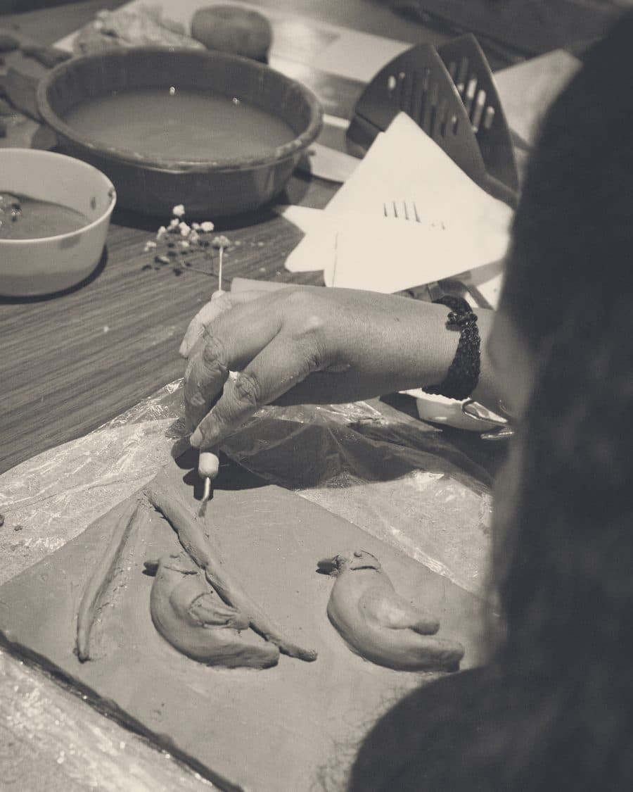Hands carving a bird into a clay tile